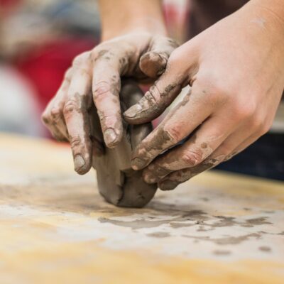 A pair of messy hands shapes a block of clay.