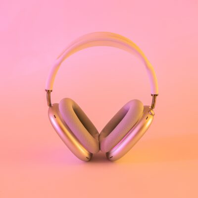 A pair of shiny, padded headphones rests against a cotton candy-like pink-and-orange background.